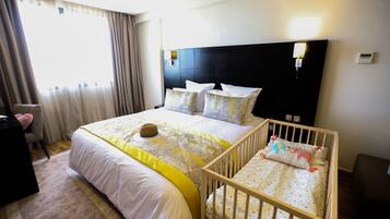 A hotel room with a large bed, a crib, a desk, and a chair.