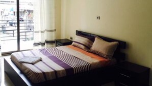 Un dormitorio con cama, mesitas de noche, una ventana con cortinas y una puerta.