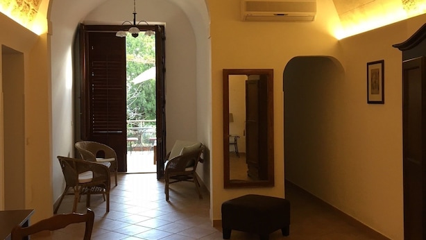 A spacious room with a high, textured ceiling, a tiled floor, and a large arched doorway leading to an outdoor area. - B&B Macrina (Noto)
