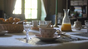 A breakfast table with a basket of bread, a cup of tea, a glass of orange juice, and a candle. - Hotel Particulier Le Ragois (Richelieu)