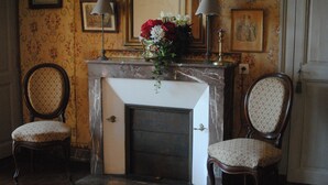 A room with a fireplace, two upholstered chairs, and floral wall decorations. - Hotel Particulier Le Ragois (Richelieu)