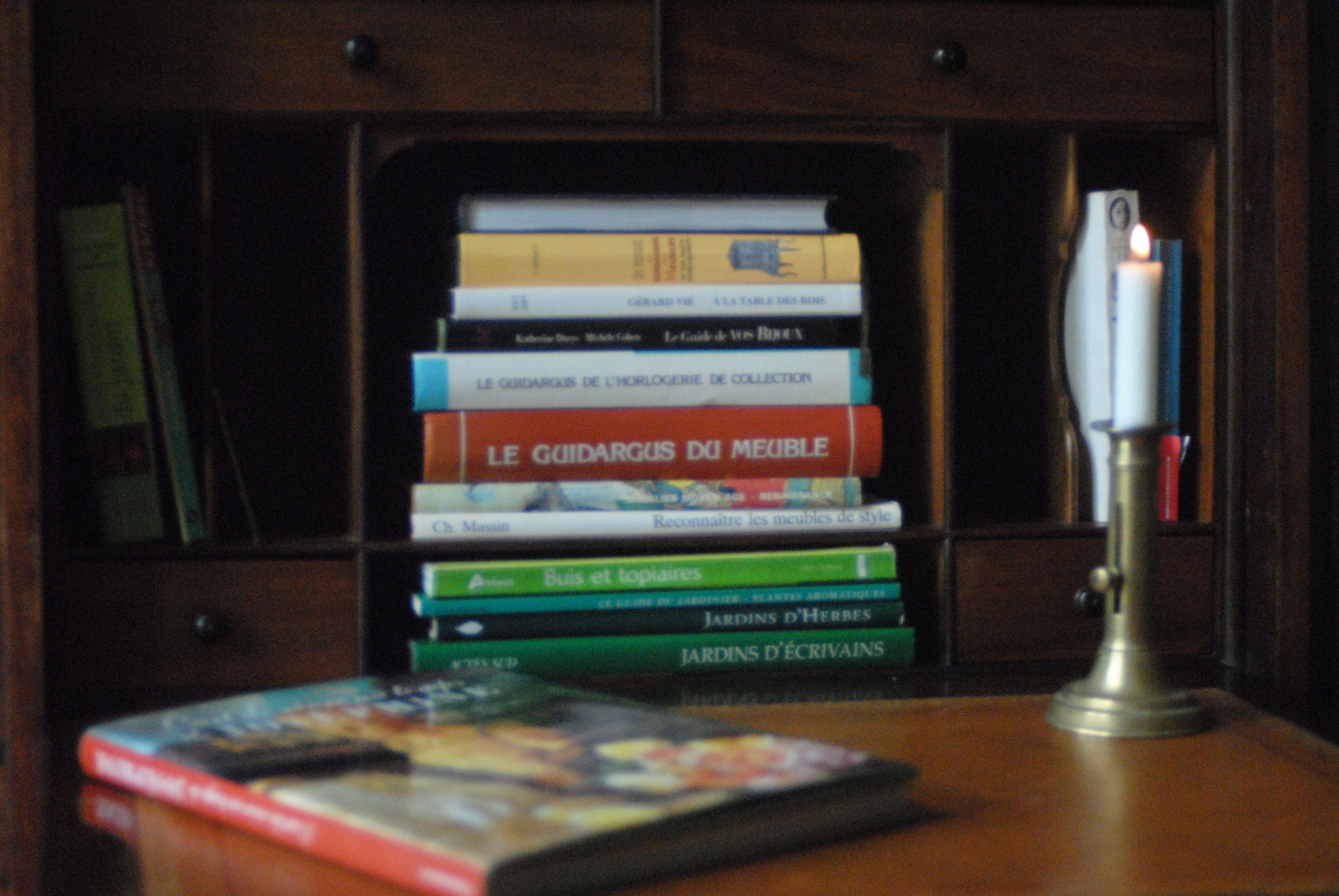 Una pila de libros sobre una estantería de madera con una lámpara de escritorio al lado.