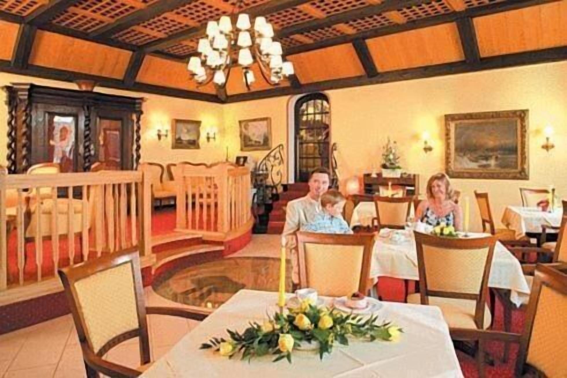 Un restaurant doté de meubles en bois, d’un lustre et d’une salle à manger où les tables sont dressées pour accueillir les clients.