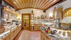A well-lit kitchen with wooden cabinets, a tiled floor, and various food items displayed on counters. - Wellness Privathotel Post an der Therme (Badenweiler)