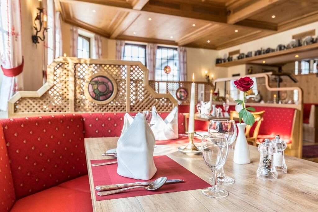 A dining area with a wooden table set for two, red upholstered seating, and a decorative partition with a floral pattern.