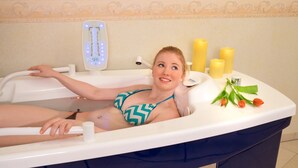 A person in a bathtub with a water jet massager, candles, and flowers on the edge. - Wellness Privathotel Post an der Therme (Badenweiler)