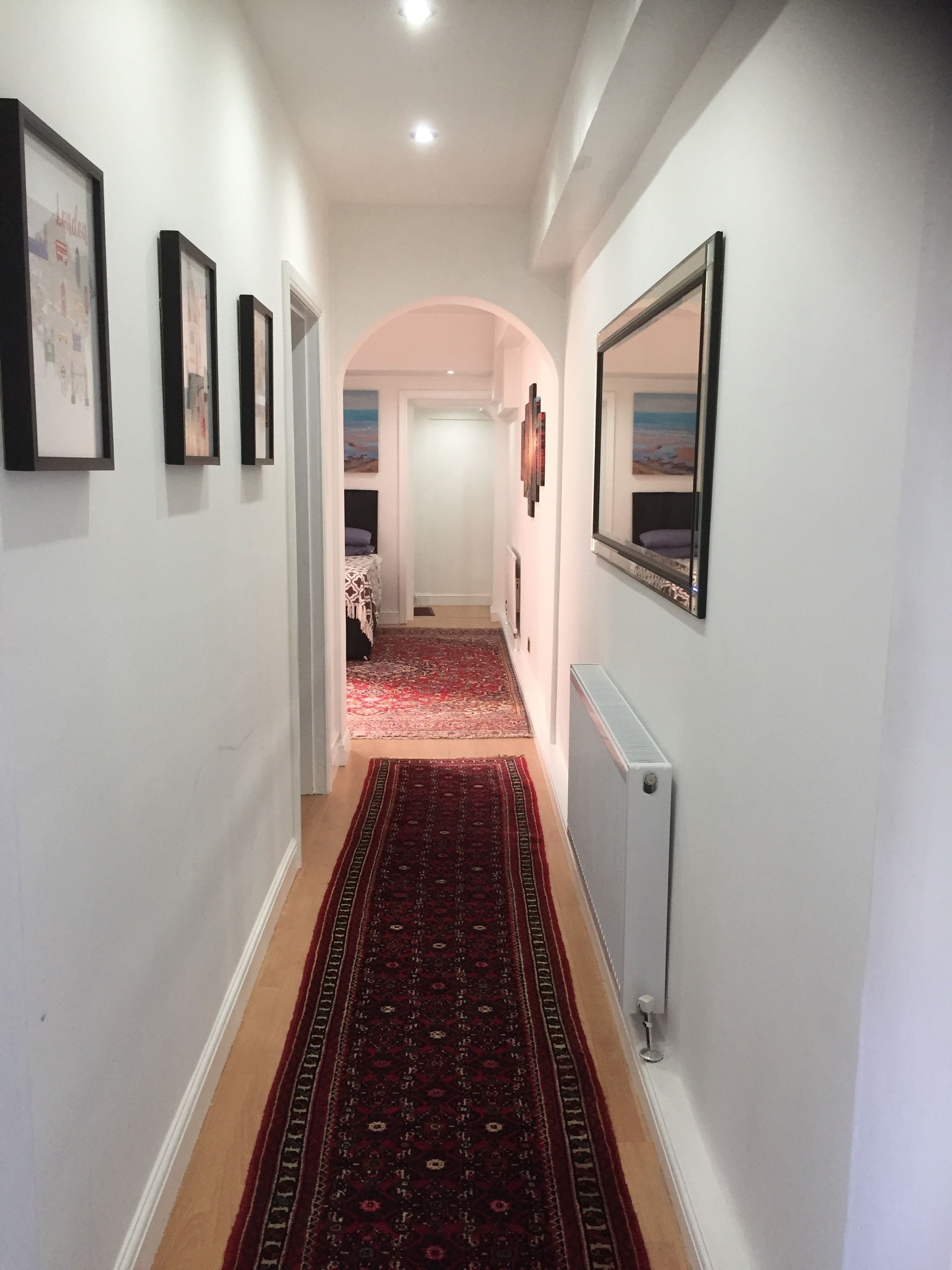 A hallway with a patterned carpet, framed pictures on the walls, and a radiator.