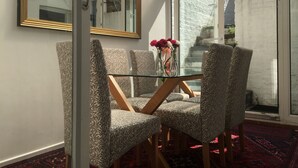 A conservatory with patterned chairs, a glass table with vases, and a view of a brick wall and stairs outside.