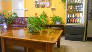 Una habitación con una mesa de madera, varias plantas en macetas, un sofá y un refrigerador lleno de bebidas.