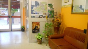 Un vestíbulo con un sofá de cuero marrón, puerta de entrada de vidrio, plantas en macetas y varios carteles informativos.