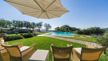 Un patio al aire libre con mobiliario de mimbre, una piscina y vistas del paisaje circundante.