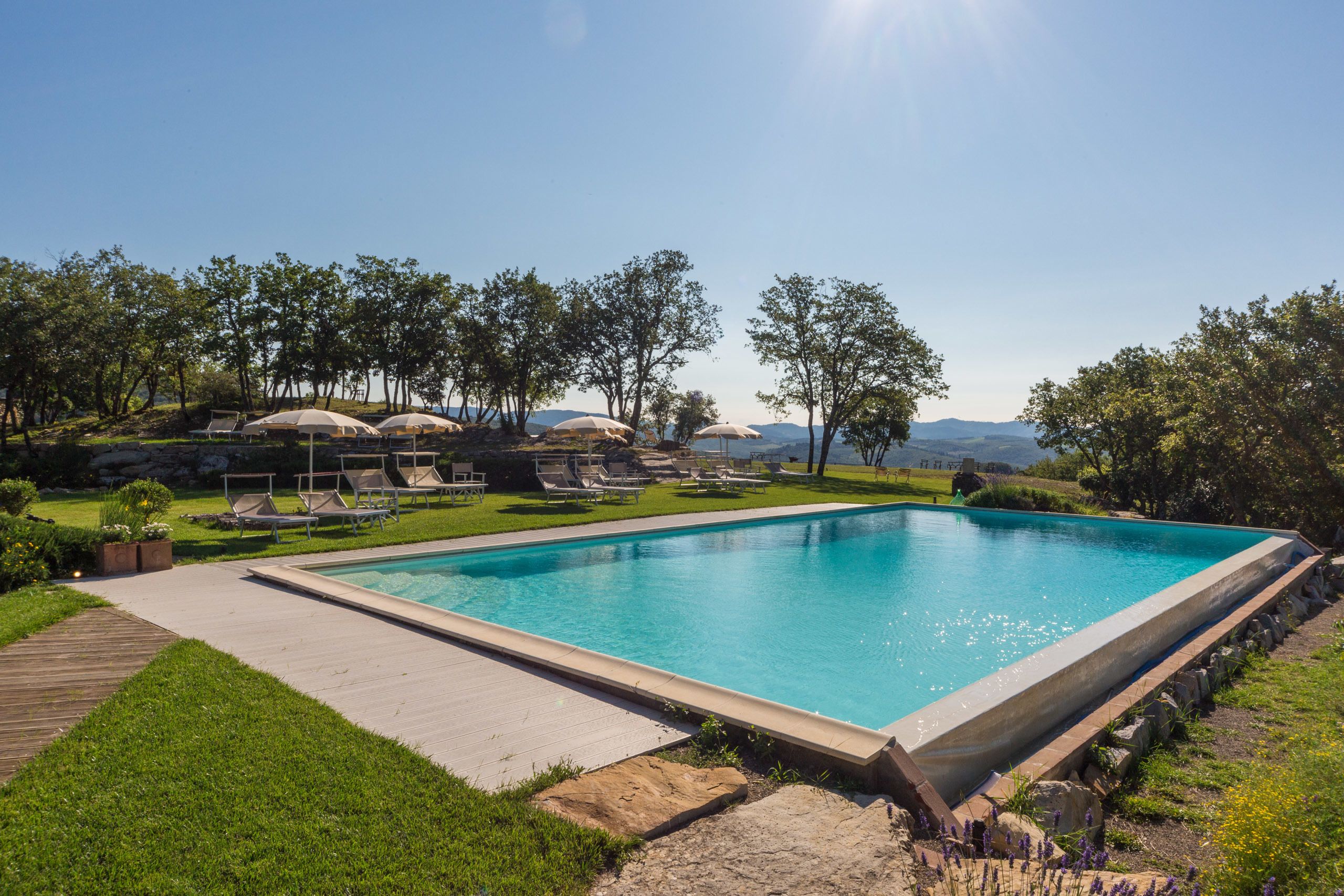 Una piscina rectangular con muelle de madera y sillas de descanso.