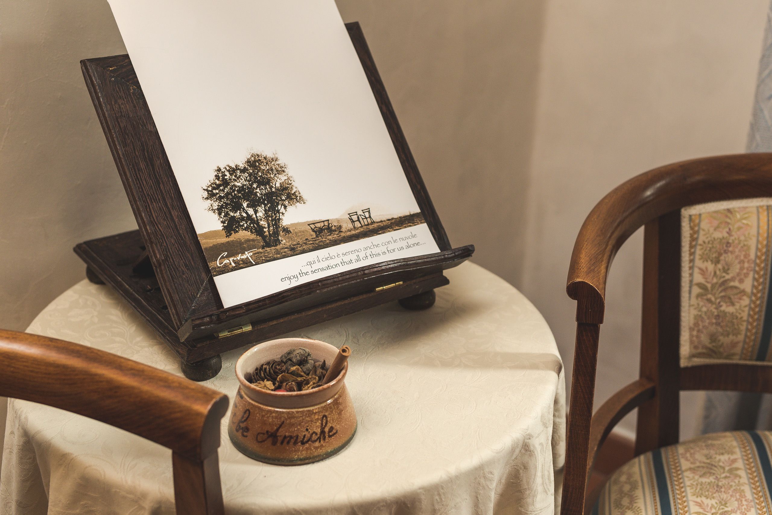 A table with a framed picture, a small bowl with tea leaves, and a chair with a floral cushion.