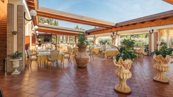 Un espace extérieur aménagé pour les repas, avec un sol en briques, des pergolas en bois et des plantes en pot.