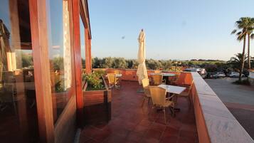 Un patio al aire libre con mesas y sillas de madera, una estatua y vistas del paisaje circundante.