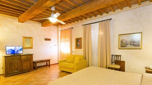 A room with a bed, a yellow armchair, a wooden cabinet, a television, and a painting on the wall. - Tenuta Elisabetta (Cecina)