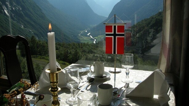 A table set for dining with a flag, candle, and mountain view. - Hotel Videseter (Stryn)