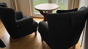 A room with two dark armchairs, a wooden table, and a large window with a mountain view. - Hotel Videseter (Stryn)