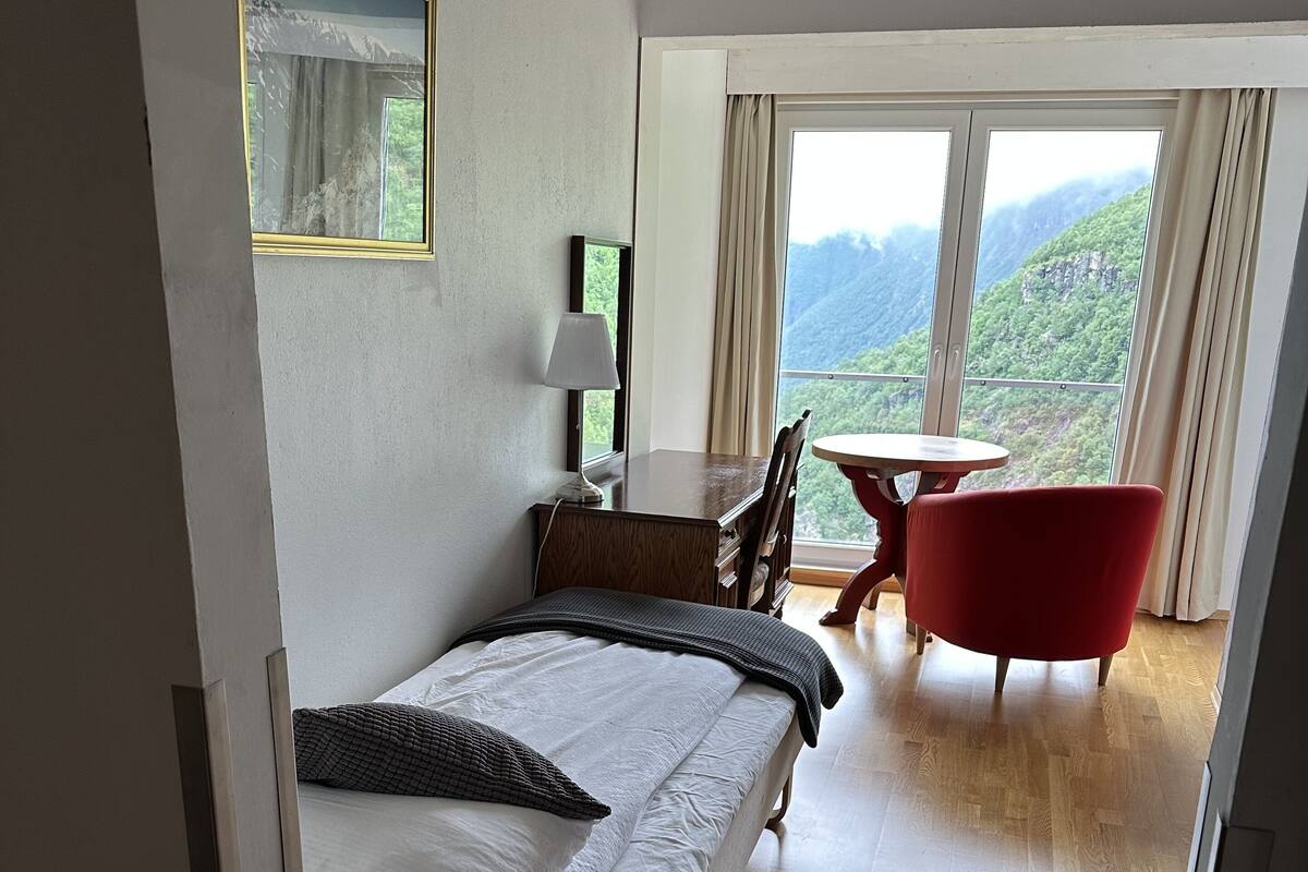 A bedroom with a bed, a desk, a chair, and a view of mountains through large windows.