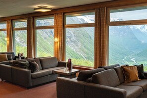 A room with a sofa and armchairs facing large windows with a mountain view.