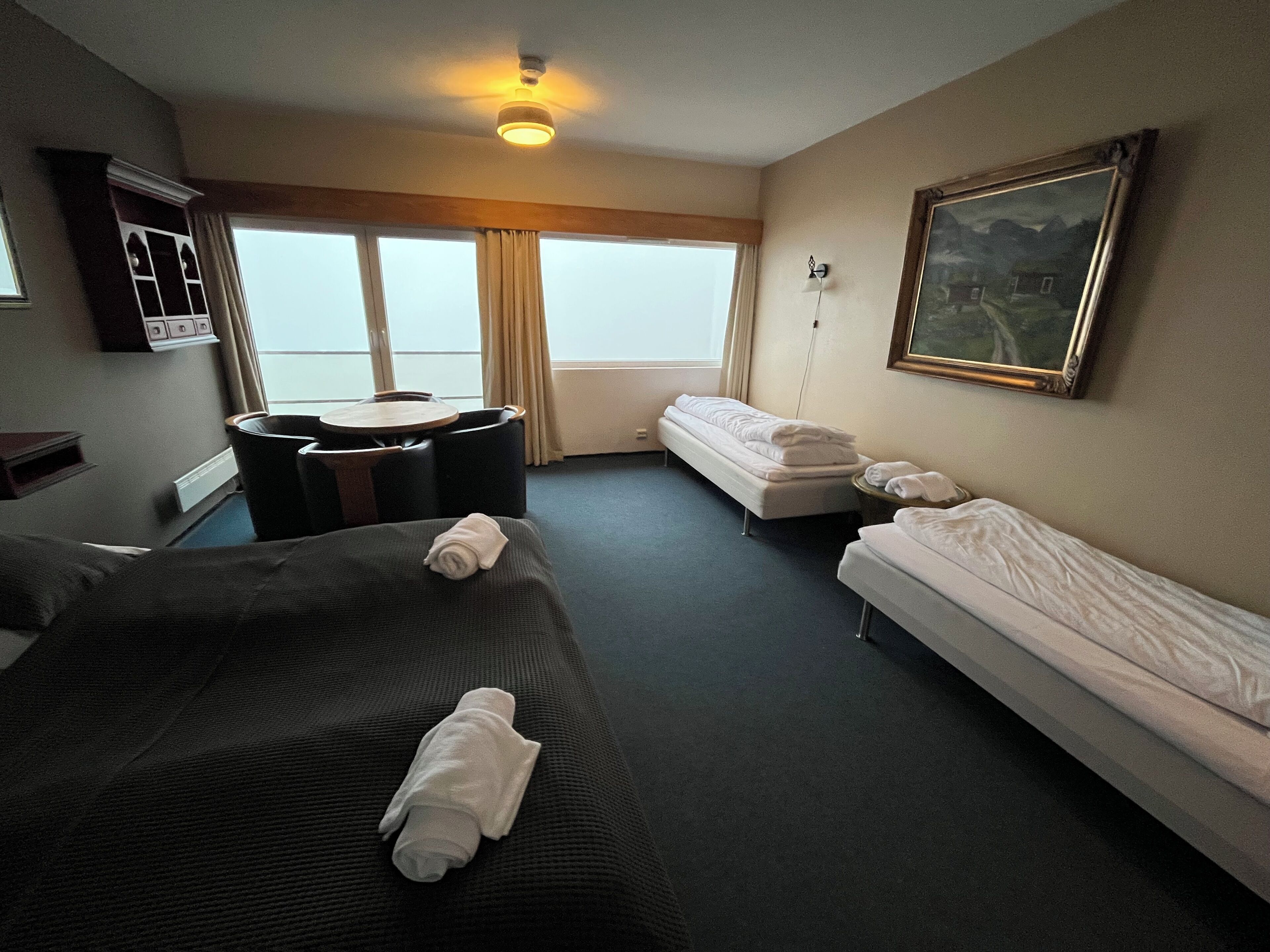 A hotel room with a large bed, a smaller bed, a sofa, a desk, and a window with curtains.