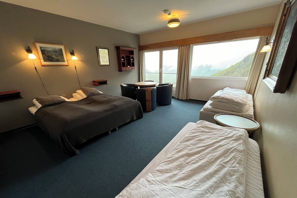 A hotel room with two beds, a small table, a chair, a cabinet, and a window with a view.