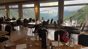 A restaurant with tables set for dining, large windows offering mountain views, and a flag on one table. - Hotel Videseter (Stryn)