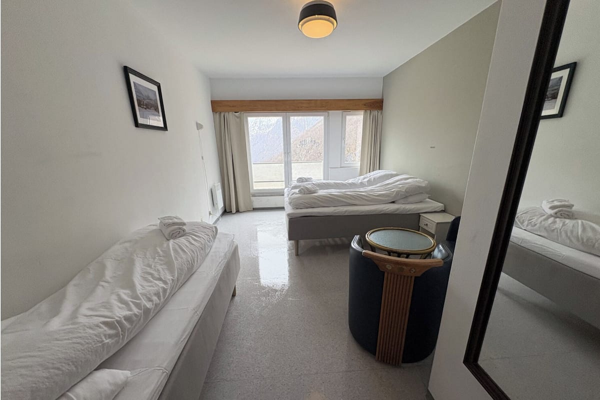A hotel room with two beds, a small round table, a mirror, and a window with curtains.