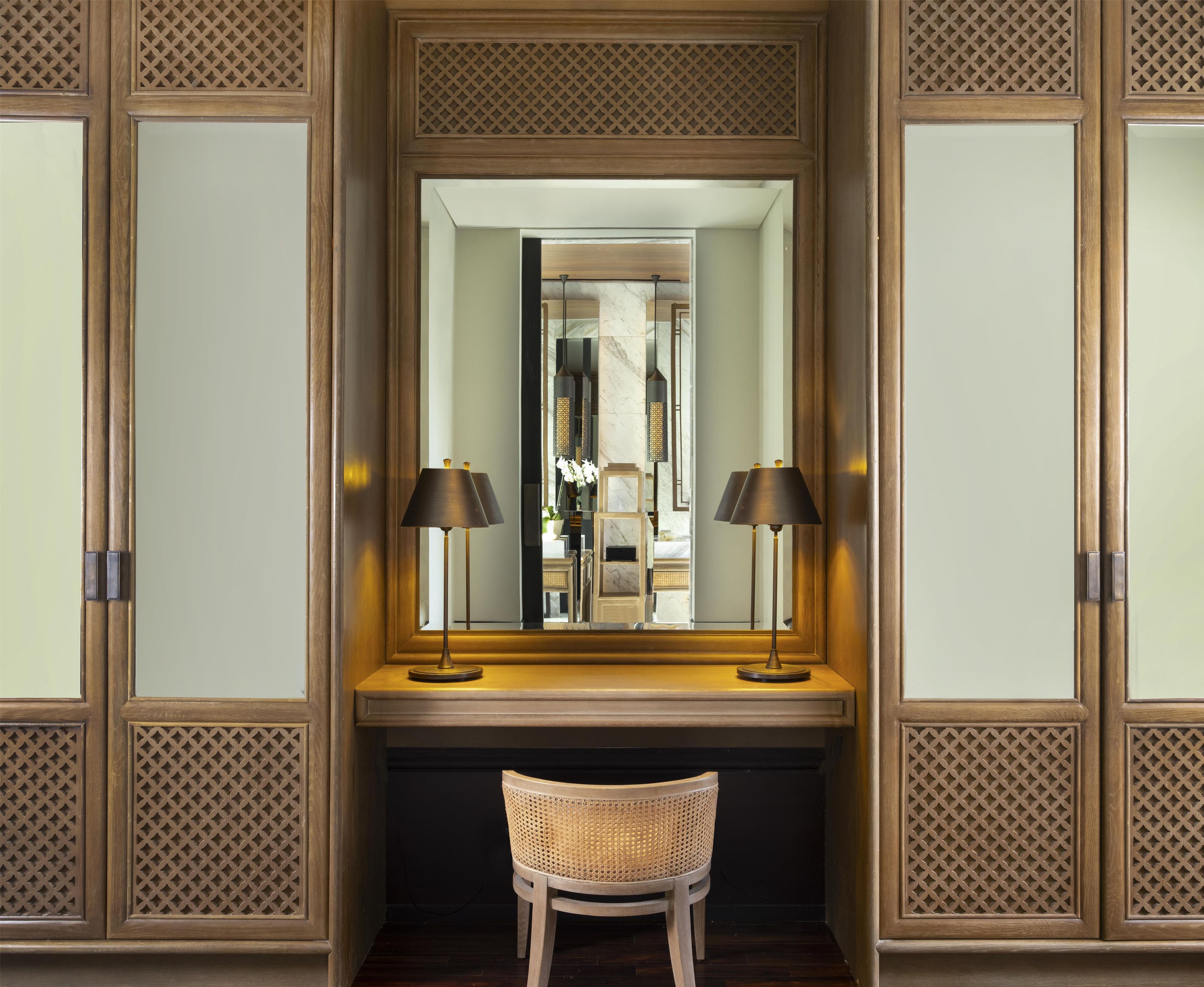 A room with a wooden desk, two lamps, a chair, and a mirror.