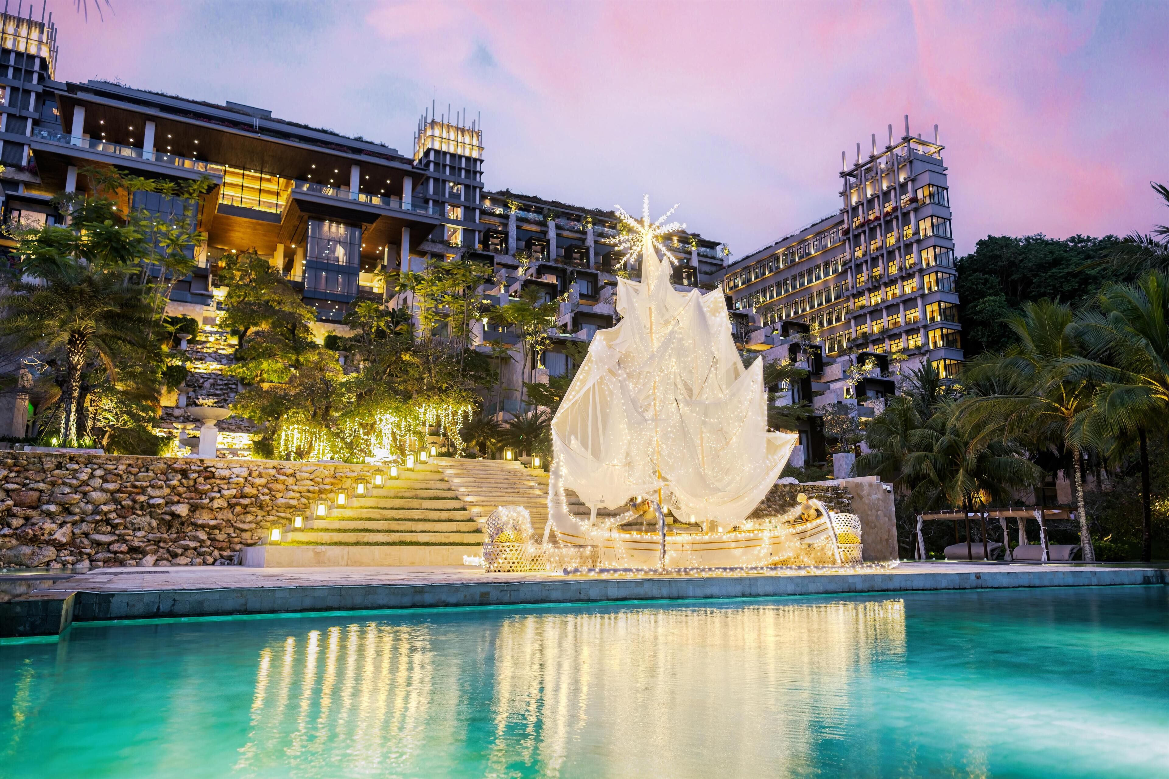 A hotel with a pool, a decorative fountain, and a view of the surrounding buildings.