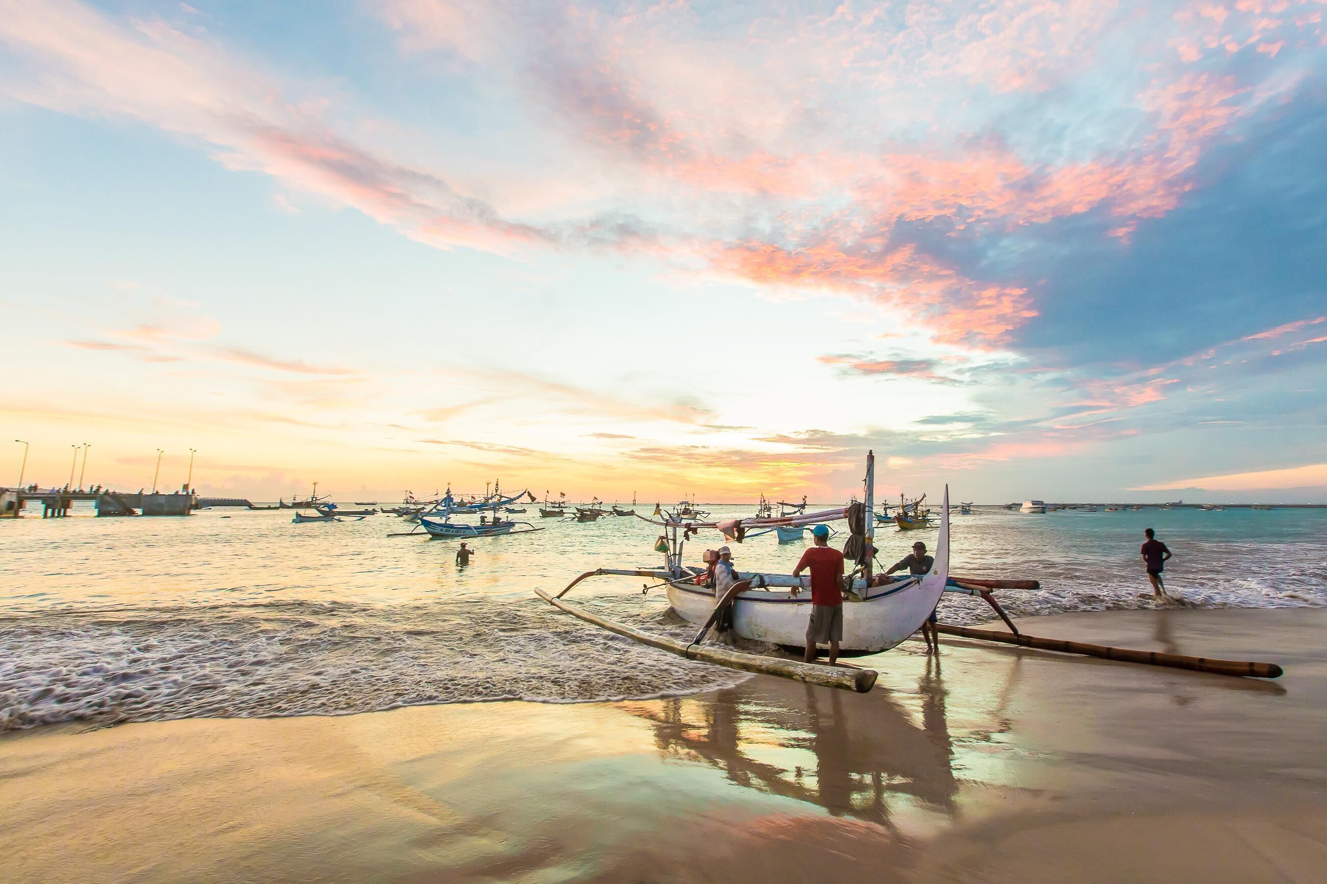A beach scene with boats and people, a pier in the background, and a sunset.