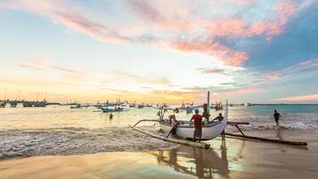 A beach scene with boats and people, a pier in the background, and a sunset.