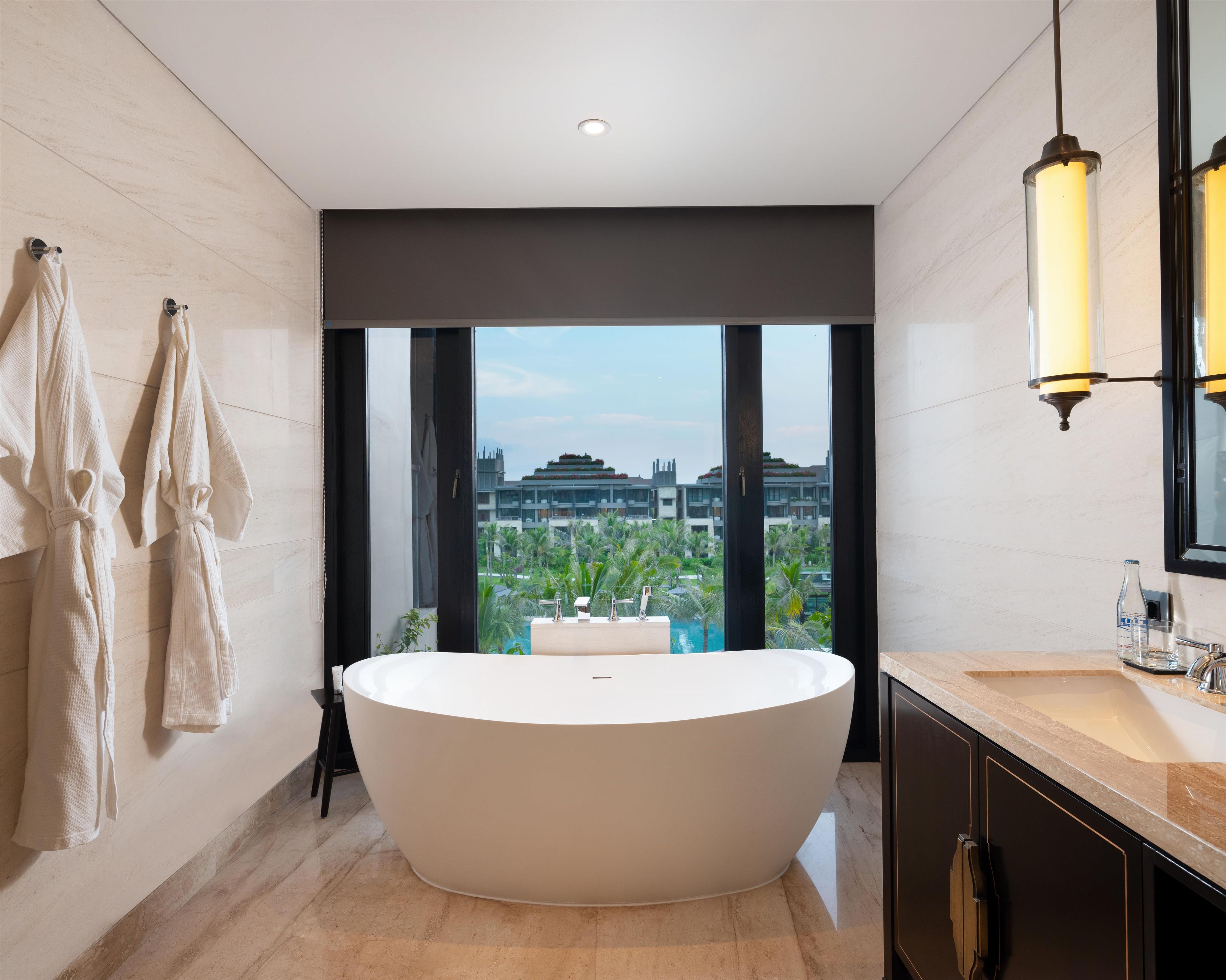 Un baño moderno con una bañera independiente grande, ducha con cerramiento de vidrio y vista a un conjunto de edificios.