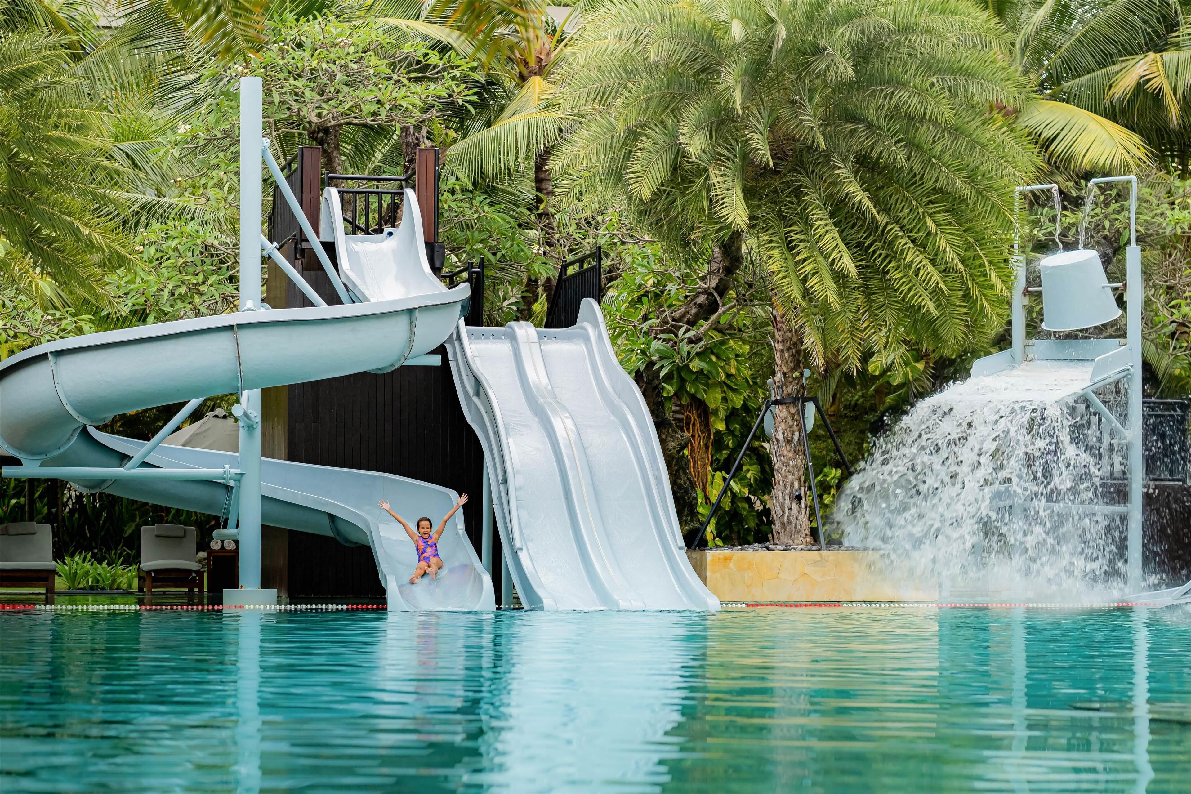 A water slide with a pool and palm trees in the background.