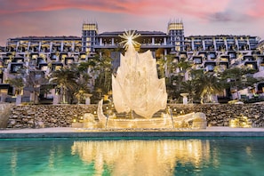 A modern hotel with a pool, a decorative fountain, and a view of the surrounding buildings.