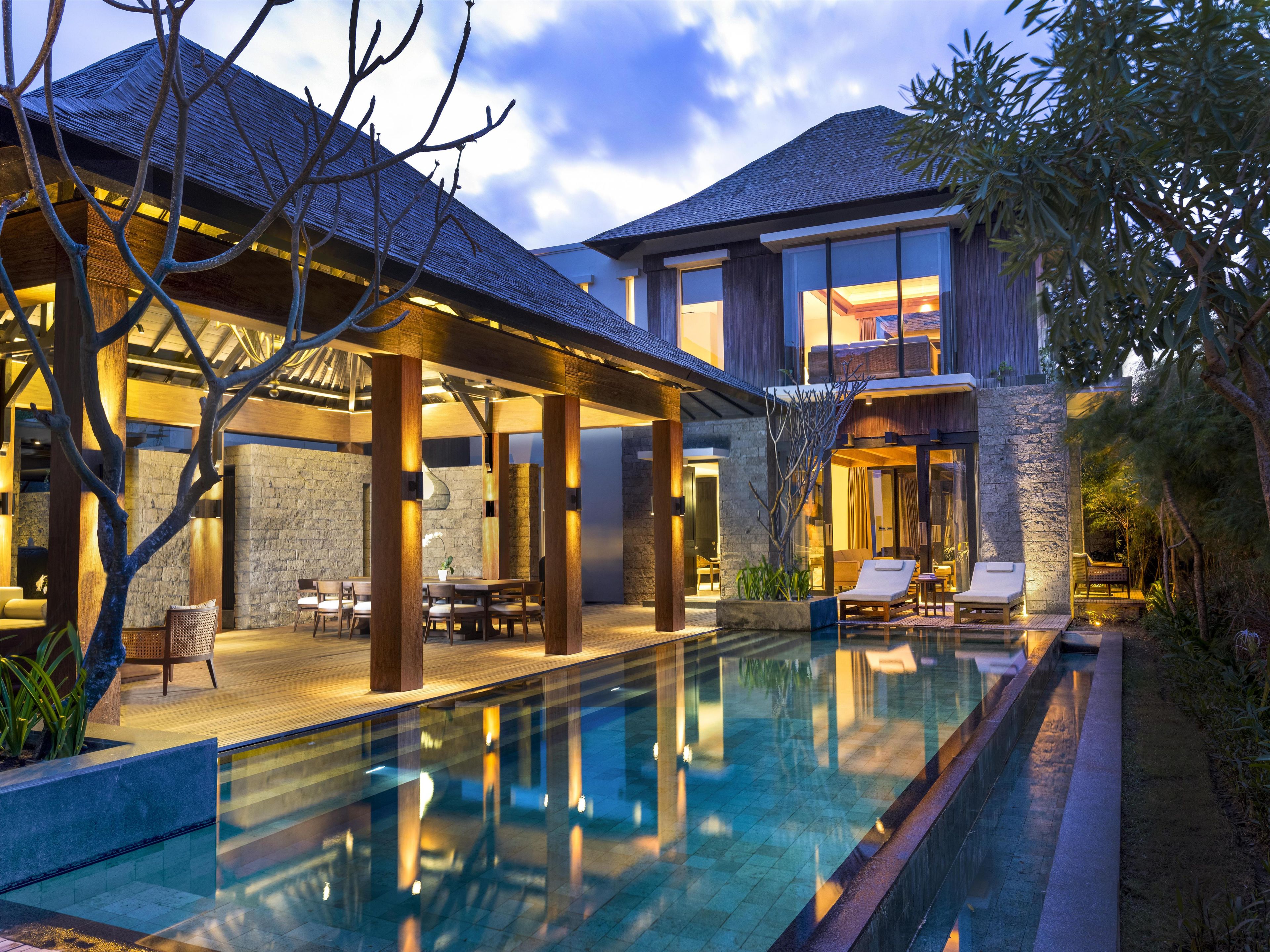 A modern house with a swimming pool, outdoor seating, and a stone wall.