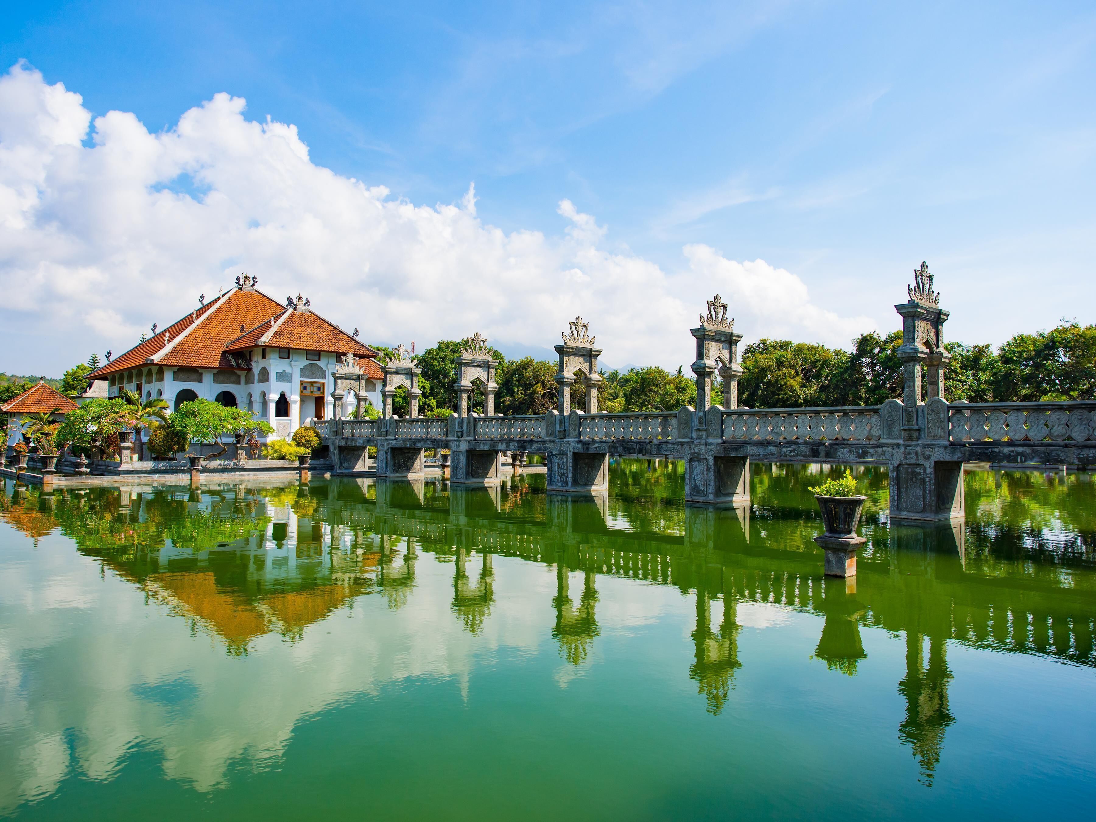 A traditional building with a tiled roof, a stone bridge with statues, and a calm water body reflecting the structure.