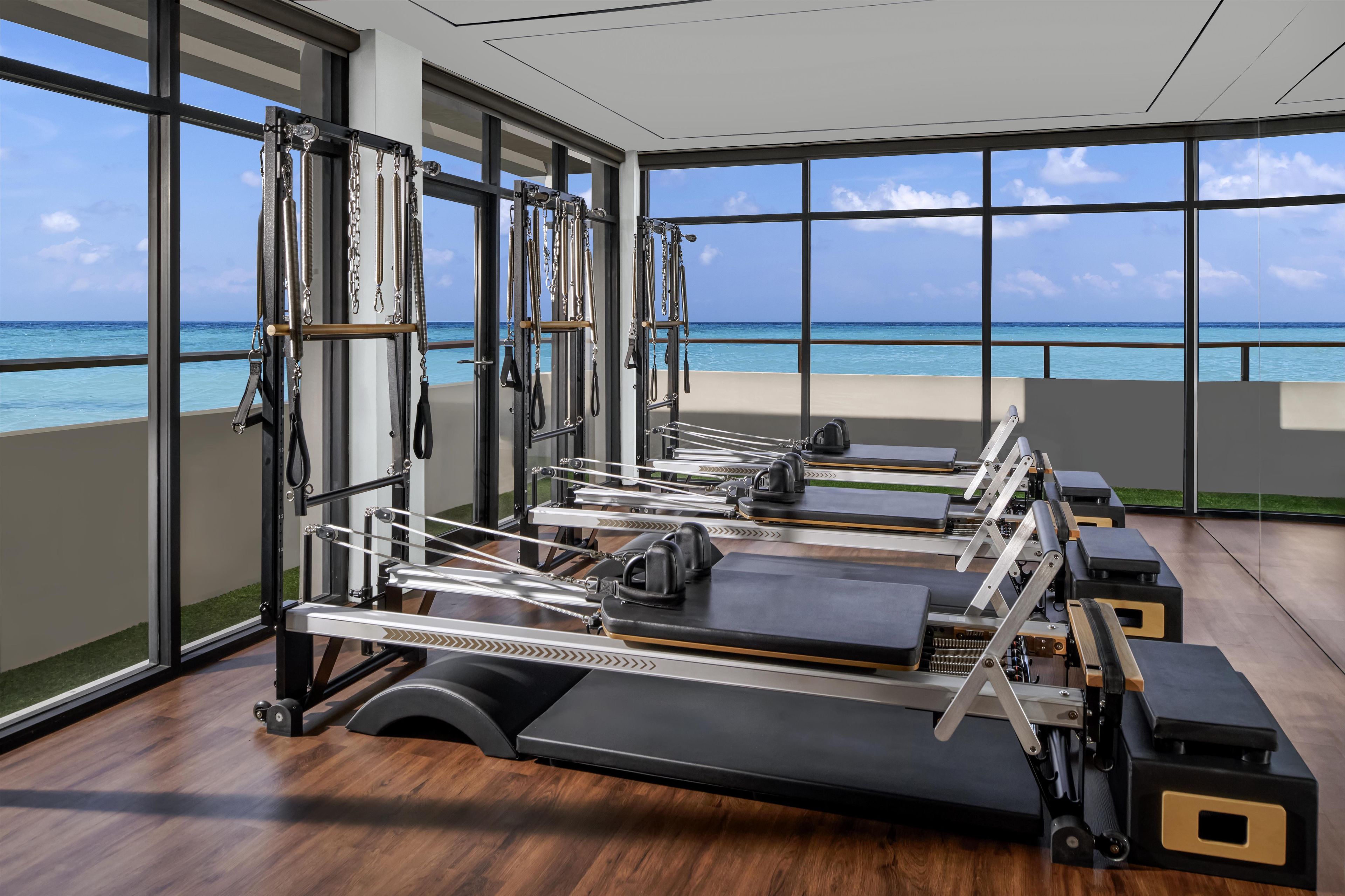 A gym with exercise equipment and large windows overlooking the ocean.