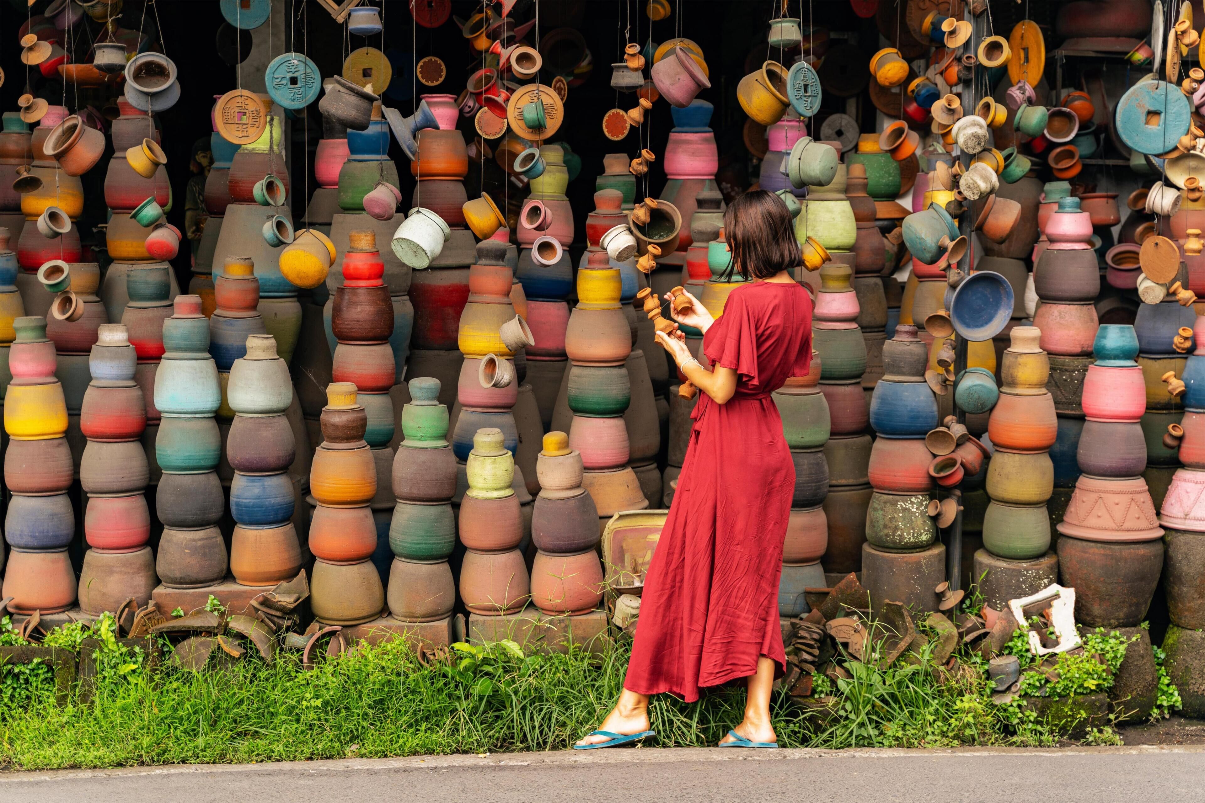 A woman examining pottery against a wall of variously shaped and sized pots.