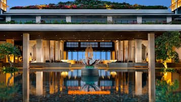 A modern hotel entrance with a reflective water feature, a seating area, and a large windowed facade.