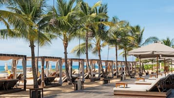 Un resort frente al mar con mobiliario de madera en terraza, palmeras y vistas al océano.