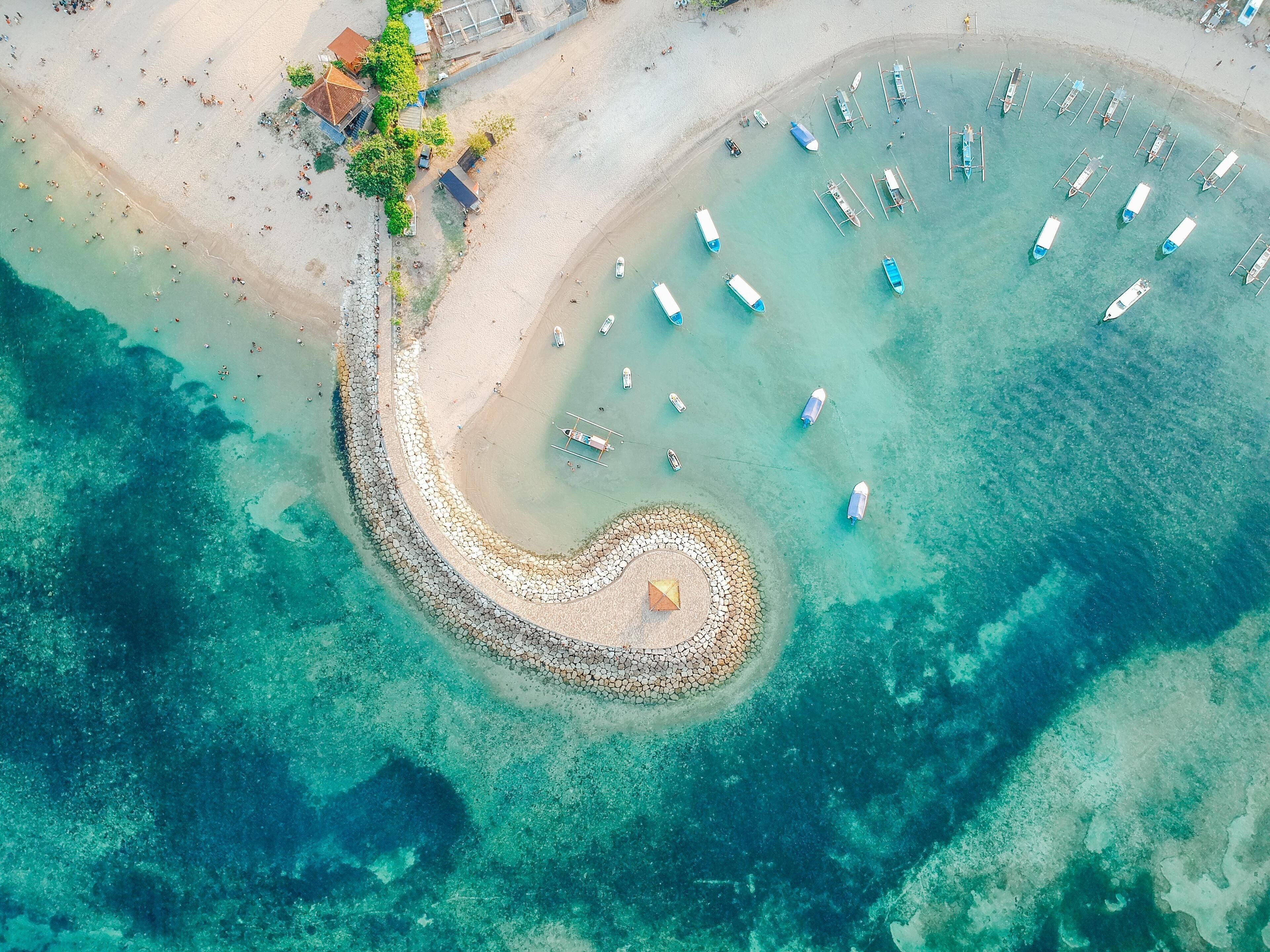 Luftaufnahme eines Strandes mit klarem türkisblauem Wasser, einem Sandufer und mehreren vor Anker liegenden Booten.