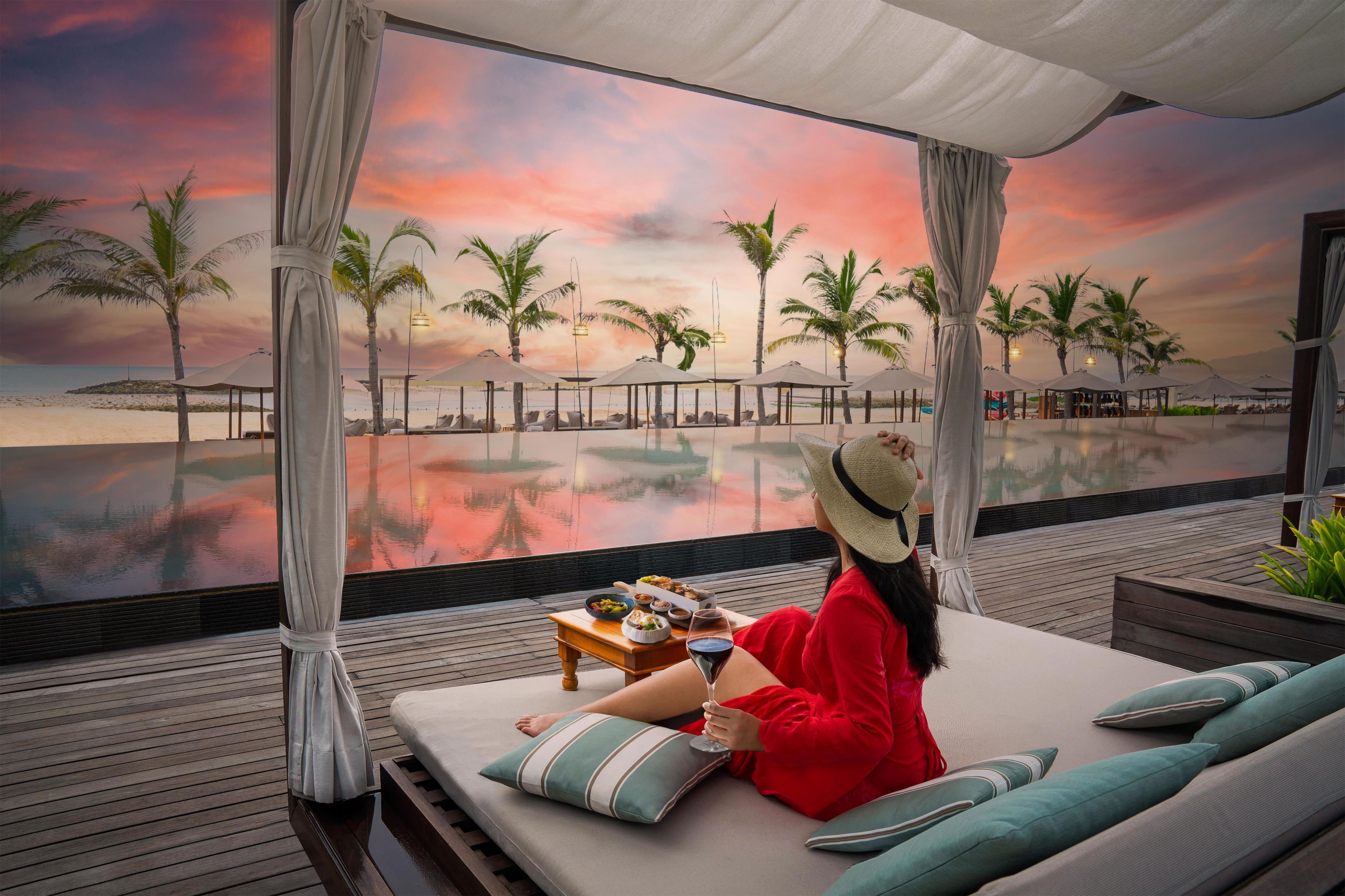 A person relaxing on a lounge chair with a view of a beach and palm trees.