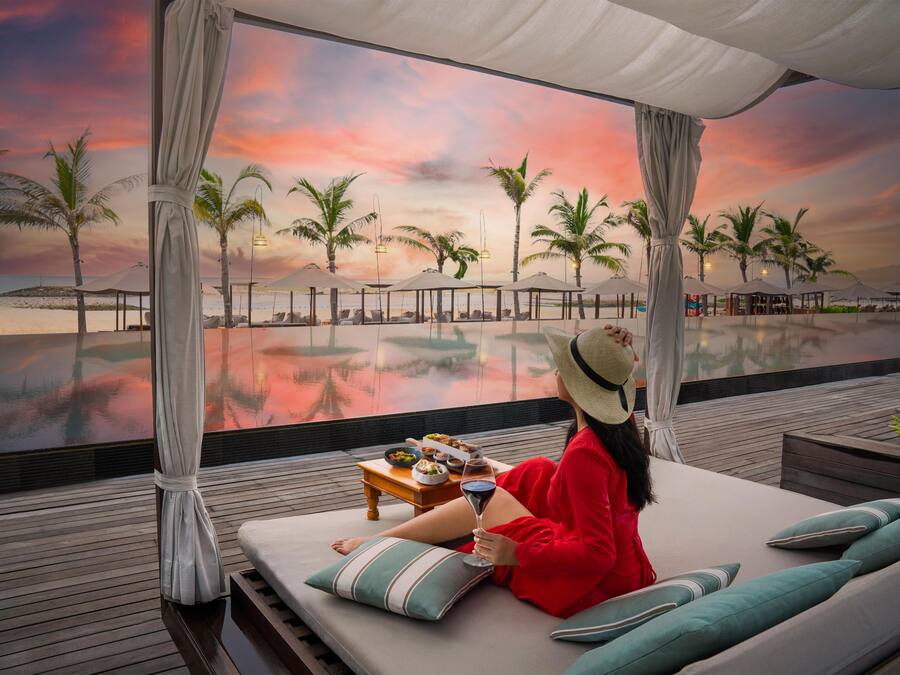 A person relaxing on a lounge chair with a view of a beach and palm trees.
