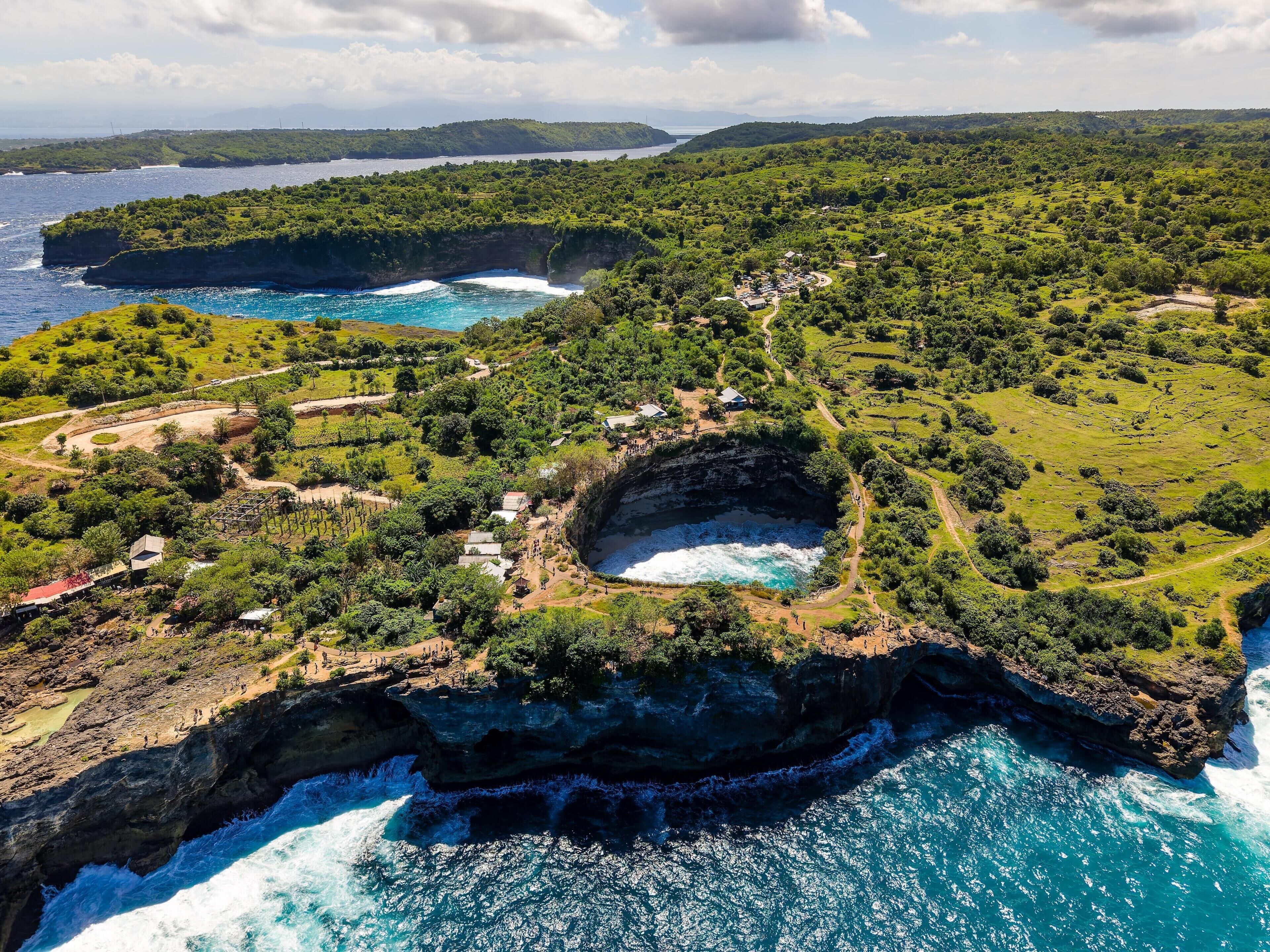 A coastal landscape with a prominent cliff, a small settlement with buildings, and a clear view of the ocean.