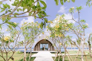 A pathway leading to a building with a unique arched roof, surrounded by greenery and overlooking a body of water.
