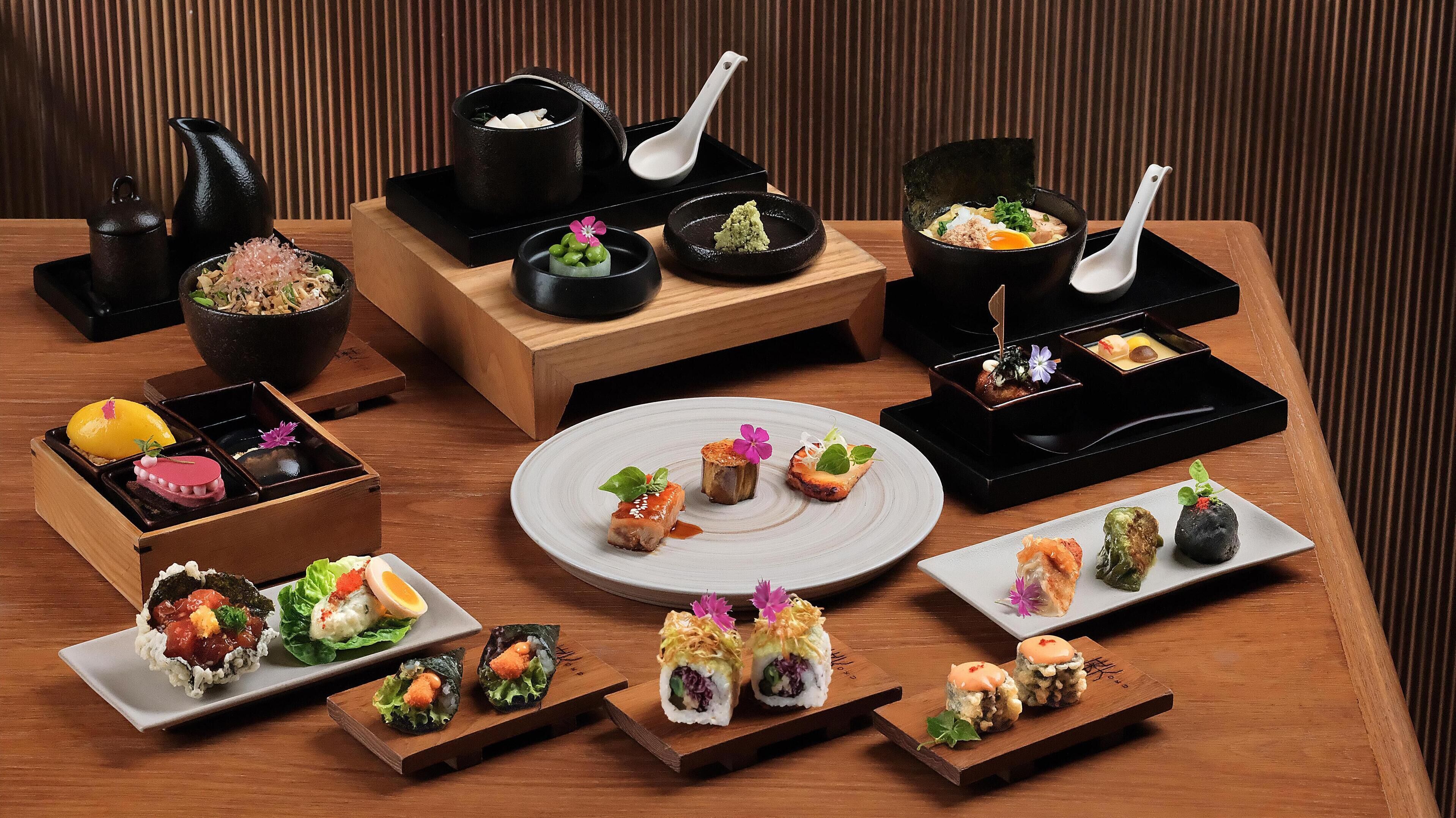 A variety of Japanese dishes arranged on a wooden table, including sushi, sashimi, and small bowls of soup.