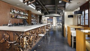 A bar area with a long counter, stools, and a wall of liquor bottles.