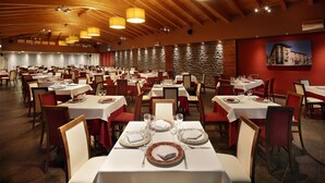 A spacious dining area with multiple tables set for dining, wooden ceiling beams, and a stone wall in the background.