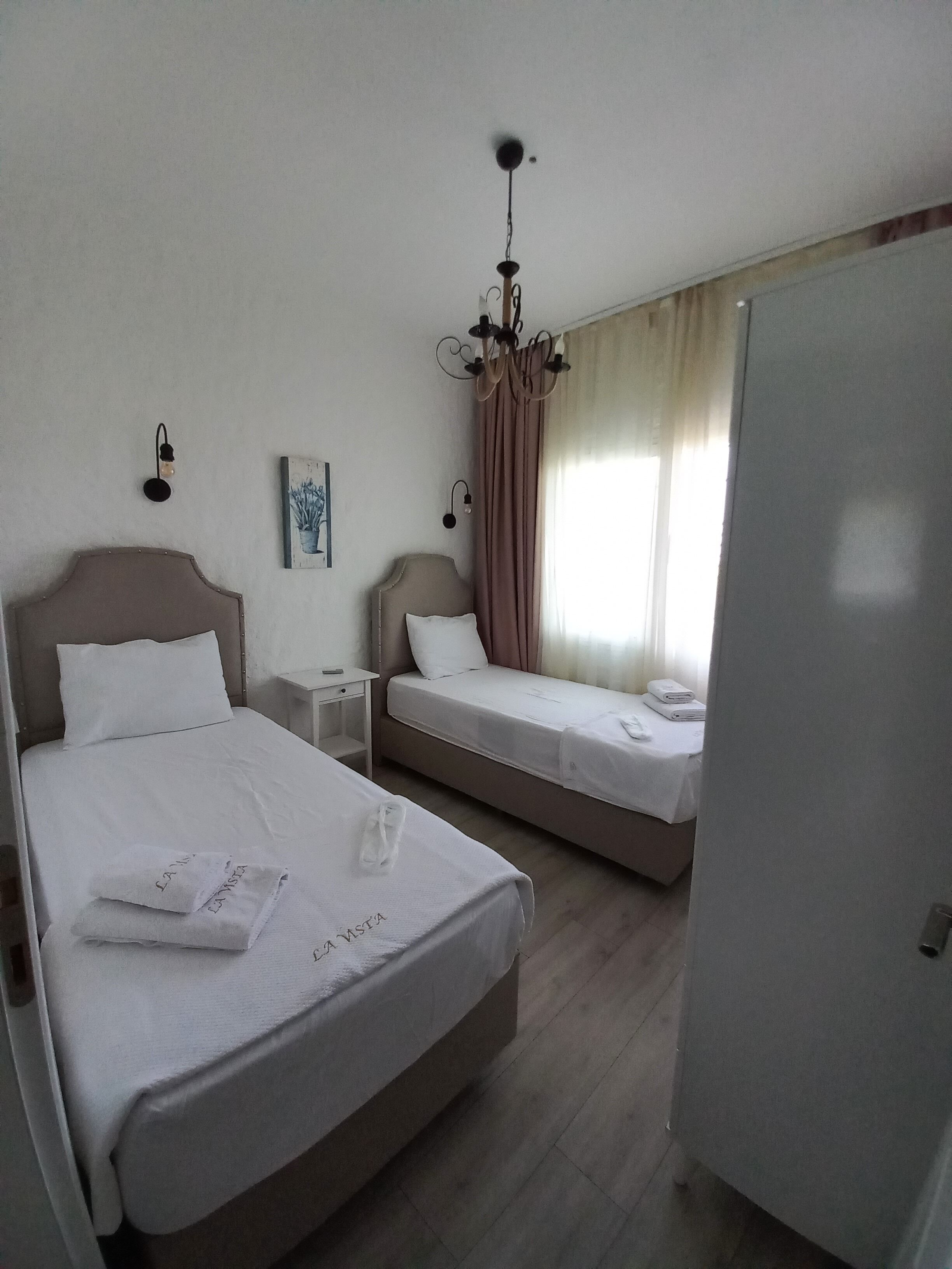 A hotel room with two beds, a chandelier, a painting, and a wardrobe.